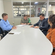 Três homens e uma mulher sentados em uma mesa de reunião. Homem com farda da Brigada Militar assina um papel