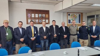 Foto horizontal colorida mostra nove homens posando para a foto na sala do pleno do conselho